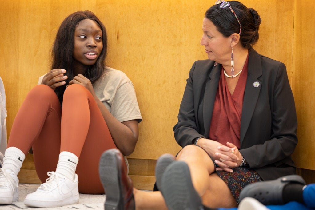 Two women talk, sitting against a wall during a break.